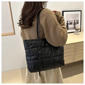 Detailed view of black quilted puffer tote bag with large square stitching and thin shoulder strap
