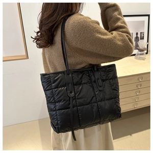 Detailed close-up of a black quilted tote bag featuring a padded square grid pattern