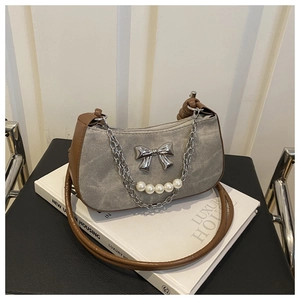 Detail of grey canvas shoulder bag featuring a silver bow charm and pearl chain accent