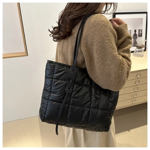 Quilted black tote bag with long straps shown on a model in a cozy indoor setting