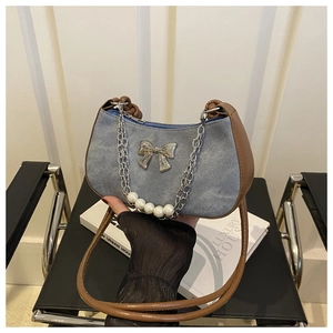 Detail of denim hobo bag featuring silver bow charm and elegant pearl chain accent