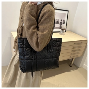 Woman carrying large black quilted tote bag with puffer padded finish on shoulder