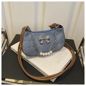 Detail of blue denim shoulder bag with brown leather strap and bow decoration