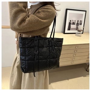 Detailed side view of black quilted tote bag with large square pattern on model