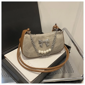 Detail of canvas shoulder bag featuring a silver bow ornament and pearl chain decoration