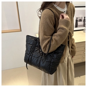 Close-up of black quilted puffer tote bag in shiny nylon worn by a female model