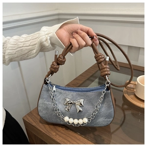 Detailed shot of denim shoulder bag featuring metal bow and faux pearl chain accent