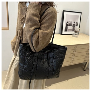 Detail of black quilted tote bag showing padded lattice texture and slim shoulder straps