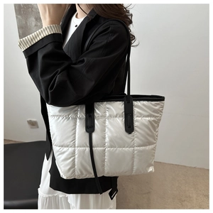 Silver quilted tote bag with black straps worn on shoulder for stylish daily commuting