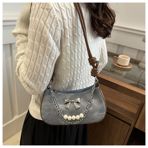 Detail of grey shoulder bag featuring metal bow, silver chain, and pearl accents