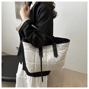 Detailed view of white quilted puffer tote bag with black straps on model shoulder