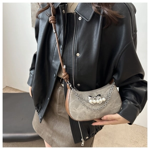 Détail du sac demi-lune en daim gris avec chaînes en métal, perles et nœud décoratif