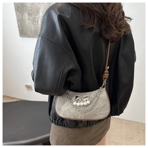 Detail of vintage grey suede crossbody bag with metal chains and pearl accents on model
