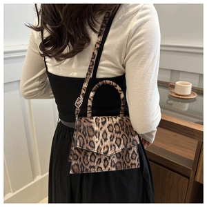 Detail of leopard print crossbody bag with round handle and adjustable strap on a model