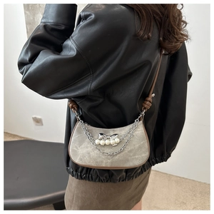 Detail of grey suede crescent bag featuring silver bow, white pearls and brown trim