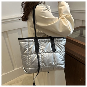 Detail of silver metallic quilted tote bag with black leather straps on a model side view