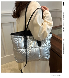 Detail of silver quilted tote bag with black straps and shiny metallic finish