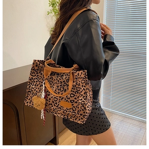 Detail of leopard print canvas tote bag with brown leather handles and plush bear charm