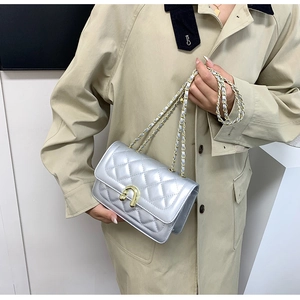 Detail of silver quilted flap bag with golden U-shaped lock and leather chain strap