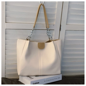 Detailed view of cream tote bag featuring metal chain straps and gold logo plate