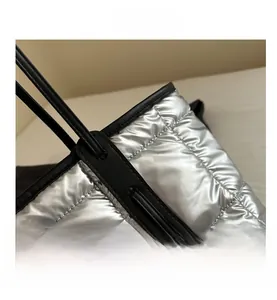Detail of silver quilted tote bag with metallic finish and black shoulder strap reinforcement