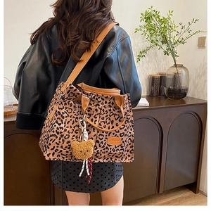 Detail of leopard print canvas tote bag featuring brown leather straps and plush bear charm