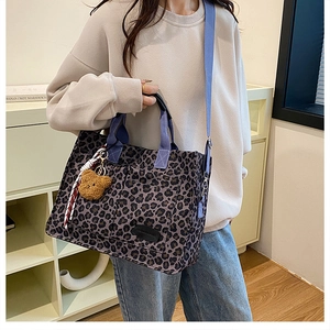 Detail of leopard print canvas tote with blue straps and plush bear charm accessory
