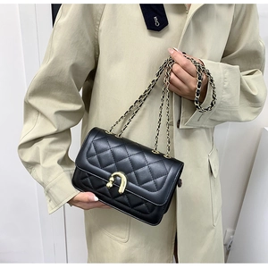 Detail of black quilted leather shoulder bag with gold U-shaped buckle on beige trench coat
