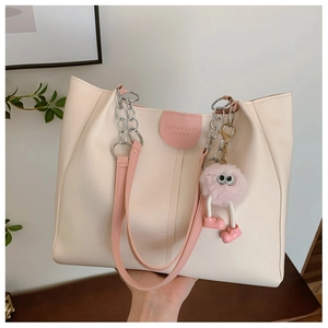 Detail of cream tote bag with pink straps, brand text and plush monster charm
