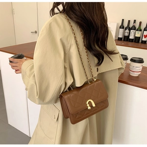 Close-up of brown quilted shoulder bag with gold arch lock and chain strap on a model