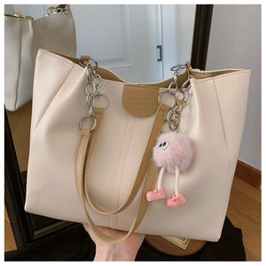 Detail of cream tote bag with chain strap, leather label, and pink plush monster charm