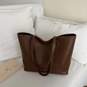 Große dunkelbraune Shopper-Tasche aus weichem Leder für Damen auf einem Sofa präsentiert