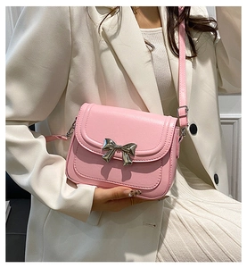 Detail of pink crossbody bag with silver bow buckle on model wearing white suit