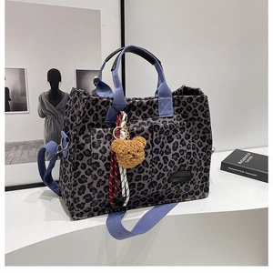 Detail view of leopard canvas tote featuring dual front pockets and plush bear charm decoration
