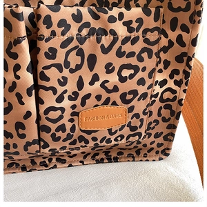 Detail of leopard print canvas tote bag featuring a leather logo patch and nylon texture
