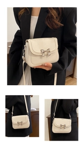 Detail view of cream crossbody bag with silver bow buckle on elegant black suit