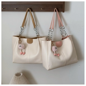 Minimalist off-white leather tote bags with contrast straps and plush charm on wood rack