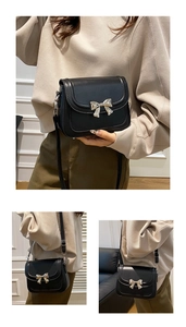 Detail of black crossbody bag with metal bow accent and slim adjustable shoulder strap