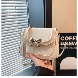 Detail of elegant cream crossbody bag featuring a stylish silver metal bow clasp