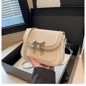 Detail view of a cream crossbody bag featuring a golden metal bow and elegant PU texture