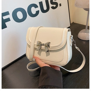 Detail of a beige mini square bag featuring a silver bow buckle and adjustable strap