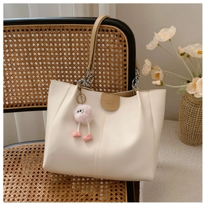 Detail of off-white leather tote bag with silver chain handles and pink plush charm