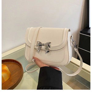 Detailed view of cream bow crossbody bag with silver buckle and smooth leather texture