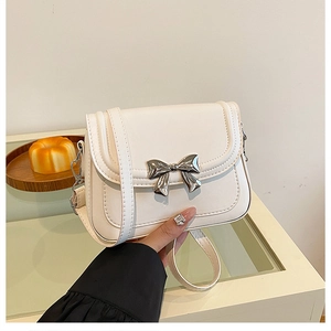 Detail of white leather shoulder bag featuring a large silver metal bow decoration