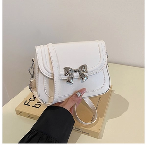 Detailed view of white crossbody bag featuring a delicate silver metal bow accessory