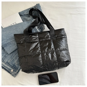 Detailed close-up of black quilted tote bag texture with puffer padding and woven handles