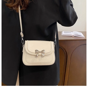 Close-up of cream crossbody bag with gold bow clasp worn with a black blazer