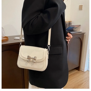 Detail of cream crossbody bag featuring a metallic silver bow clasp and leather texture