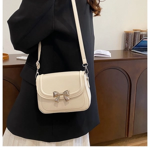 Detailed view of cream leather crossbody bag featuring a silver metal bow ornament