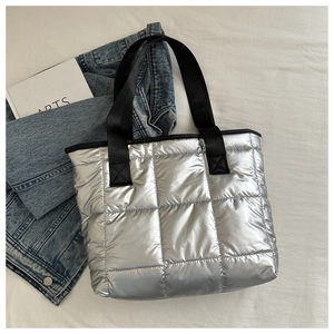 Detailed view of silver quilted tote bag with black straps on a white textured backdrop
